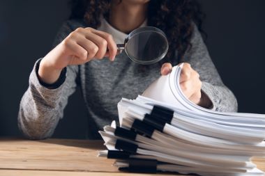woman holding magnifying glass and documents.