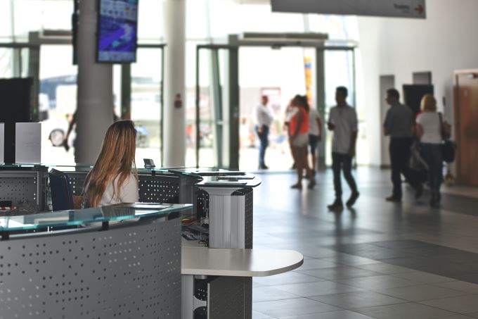 A female receptionist sitting at a reception desk in a corporate building filled with passersby