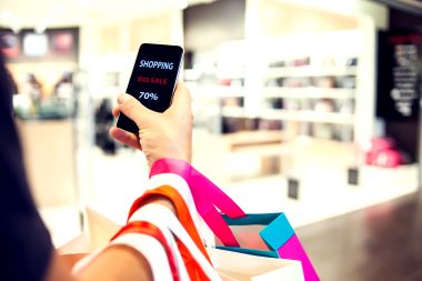 近景照片，男子手中拿着购物袋和手机，手机上有「网上购物」字样。