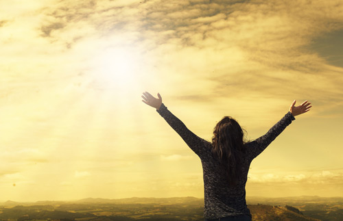 A person watches the sun with arms spread wide 