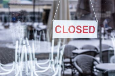 Sign saying closed hanging on the glass door of a restaurant or a bar.