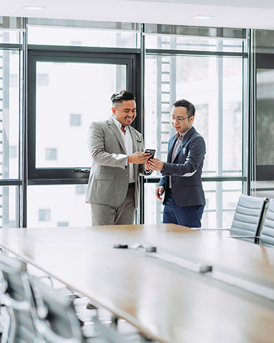 Two Asian men checking a smartphone together in a meeting room